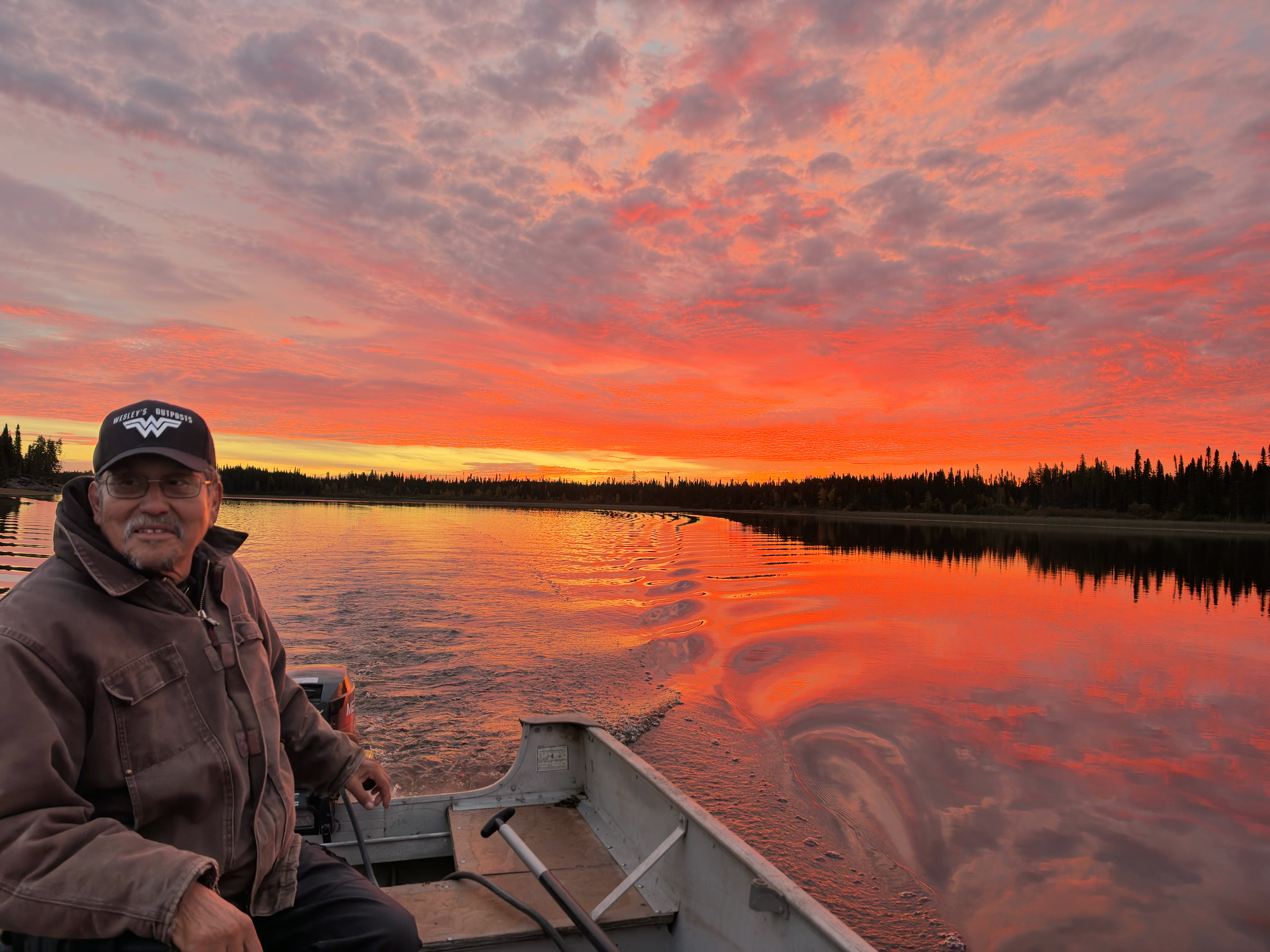 Charles Wesley riding in a boat on a northern Ontario river beneath a vivid morning sunrise