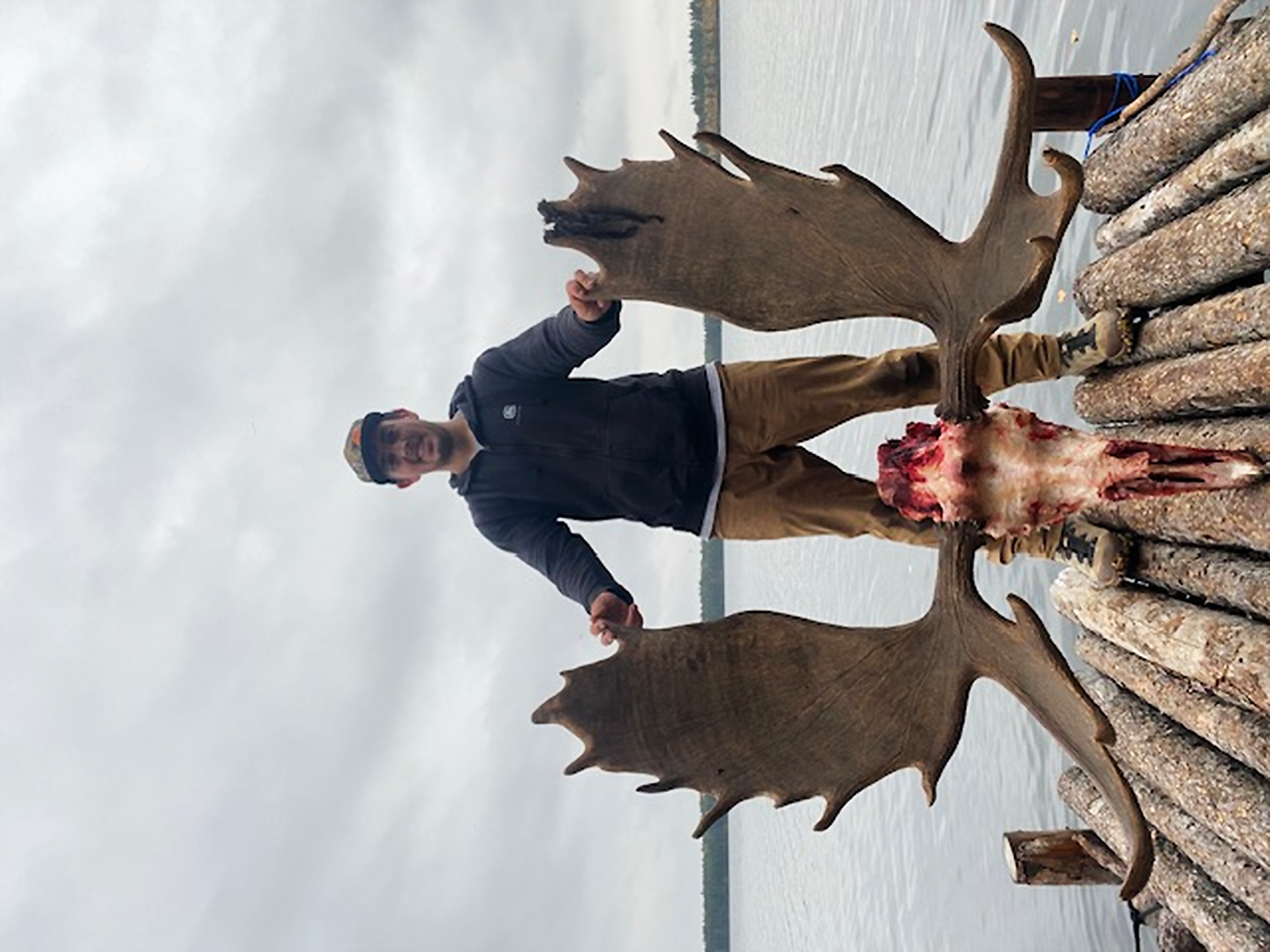 Non-Ontario resident hunter holding a moose skull and rack on a dock after a successful tent-camp hunt